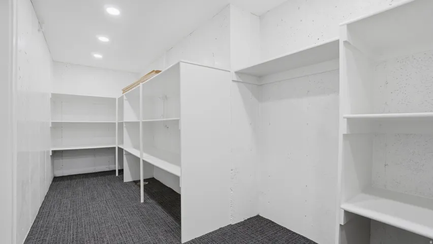Spacious storage area featuring extensive built-in shelving, recessed lighting, and carpet flooring