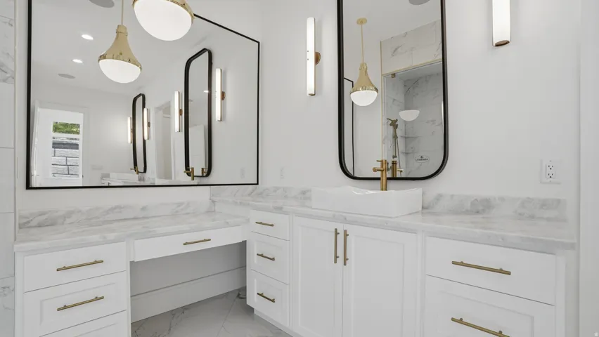 Bathroom vanity featuring white cabinetry with brass hardware, a contrasting white vessel sink, and a large wall-mounted mirror