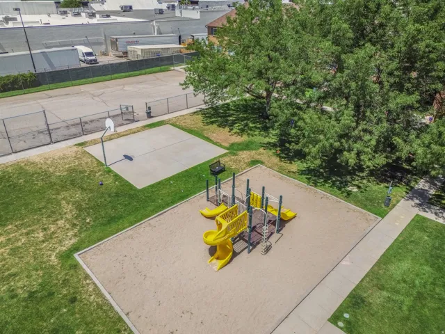 Recreational area featuring a sand-based playground structure with yellow slides, a concrete basketball half-court, and expansive green spaces