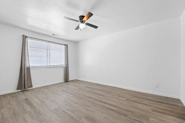 Room featuring vinyl wood-finish flooring, a ceiling fan with integrated lighting, and a large window with horizontal blinds