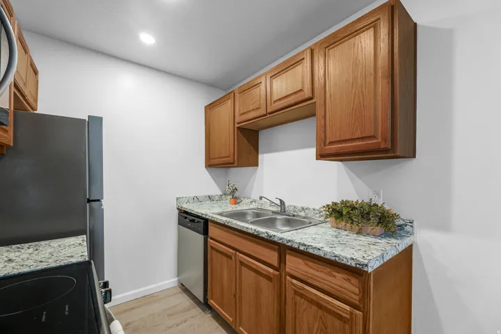 Kitchen featuring wood cabinetry, light-colored speckled countertops, a double basin stainless steel sink, and stainless steel appliances