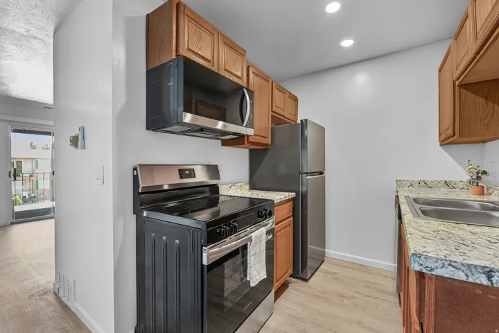 Kitchen featuring wood-finish cabinetry, granite-style countertops, and stainless steel appliances including a range with an overhead microwave, and a refrigerator