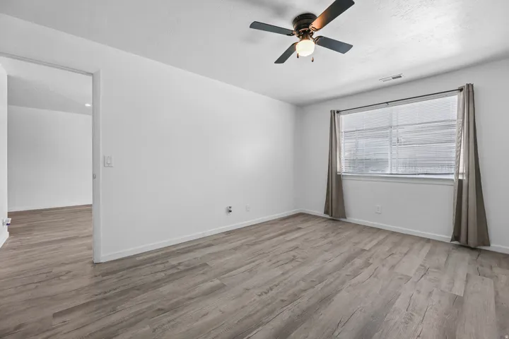 Room featuring vinyl wood-finish flooring, white walls, and a ceiling fan with integrated lighting