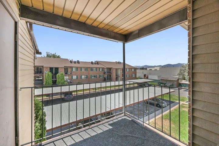 Private balcony with a metal railing, overlooking covered parking and distant mountains