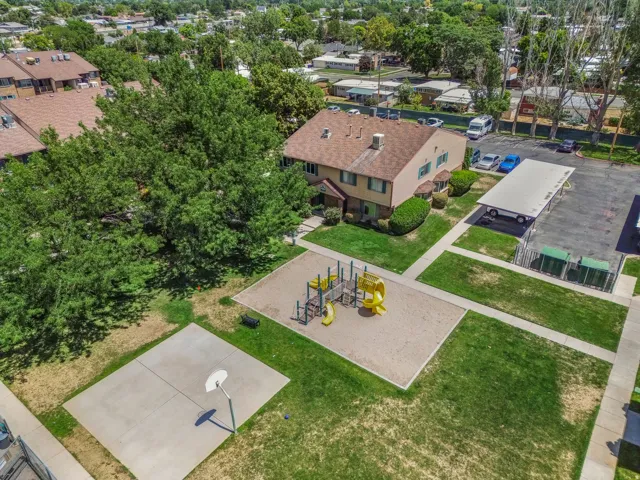 Community green space featuring a sand-based play area with equipment, a concrete sports court with a basketball hoop, and manicured lawns