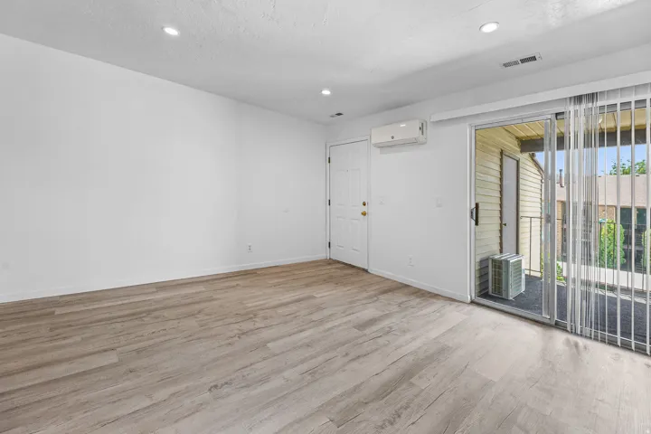 Spacious room featuring wood-finish flooring, recessed lighting, and a sliding glass door to an exterior balcony