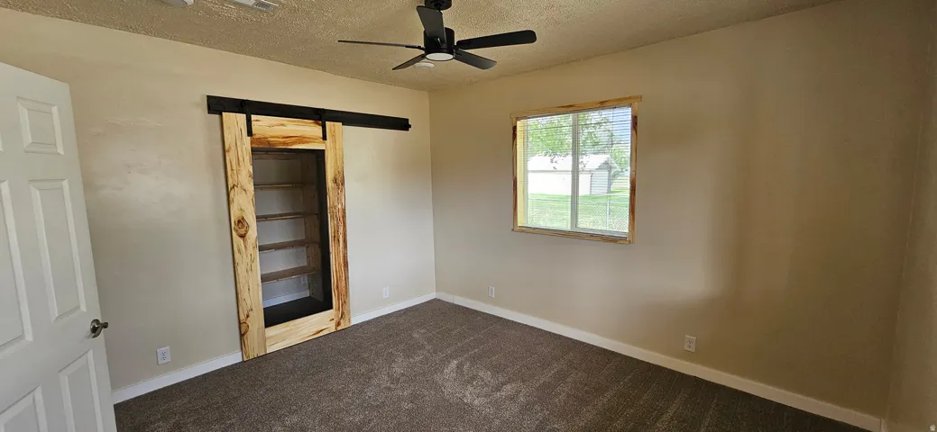 Bedroom featuring neutral-toned walls, dark carpet flooring, and a ceiling fan with integrated lighting