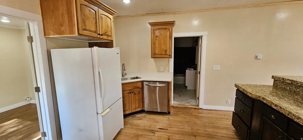 Kitchen featuring wood-finish flooring, natural wood cabinetry, light-toned countertops, and a stainless steel dishwasher