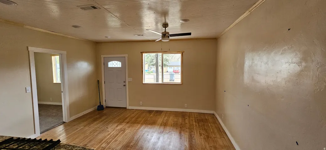 Spacious room featuring wood-finish flooring, a white paneled front door with an arched lite, and a ceiling fan