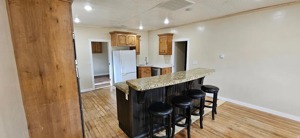 Open-concept kitchen featuring an island with a stone-finish countertop, wood-finish flooring, recessed lighting, and wood cabinetry