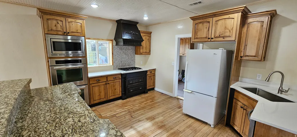 Bright kitchen featuring wood-finish flooring, light-toned cabinetry, stainless steel appliances, a built-in oven and microwave, and white countertops