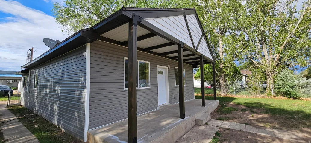 Exterior featuring gray horizontal siding, a covered concrete porch, white trim, and a black roof