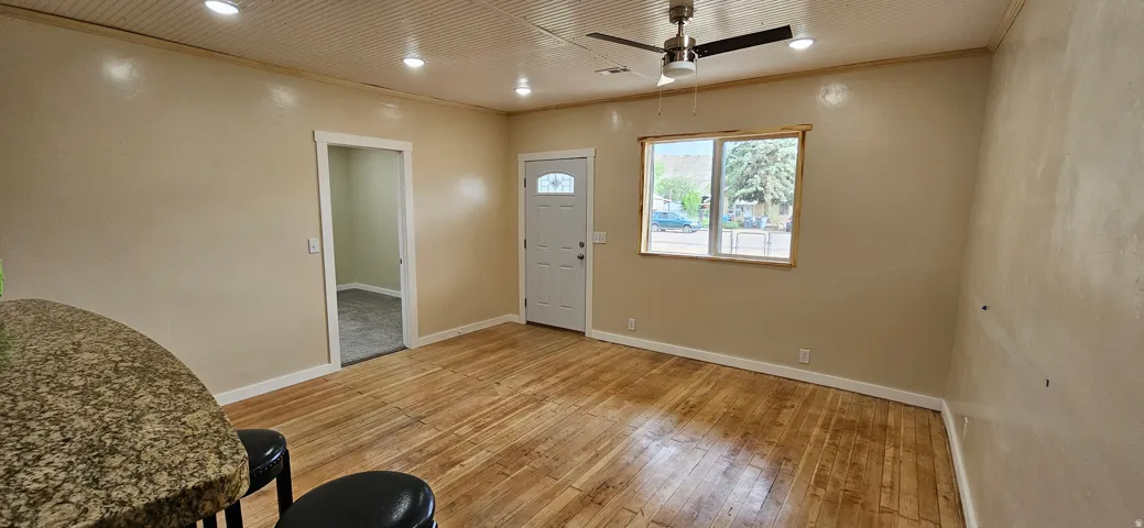 Room featuring wood-finish flooring, a white paneled entry door with decorative glass, and a ceiling fan with integrated lighting