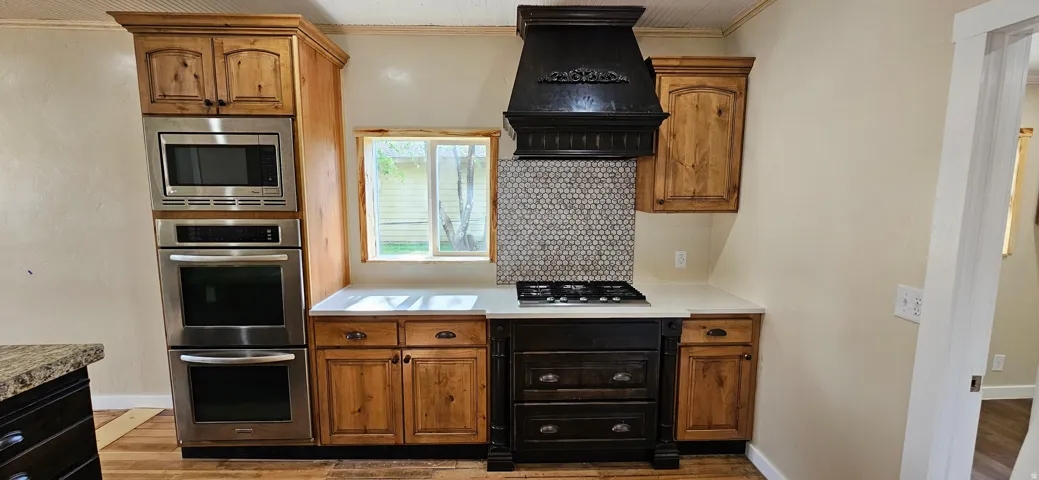Kitchen featuring a built-in stainless steel double oven and microwave combination, a gas cooktop, a dark wood custom range hood, and a mosaic tile backsplash