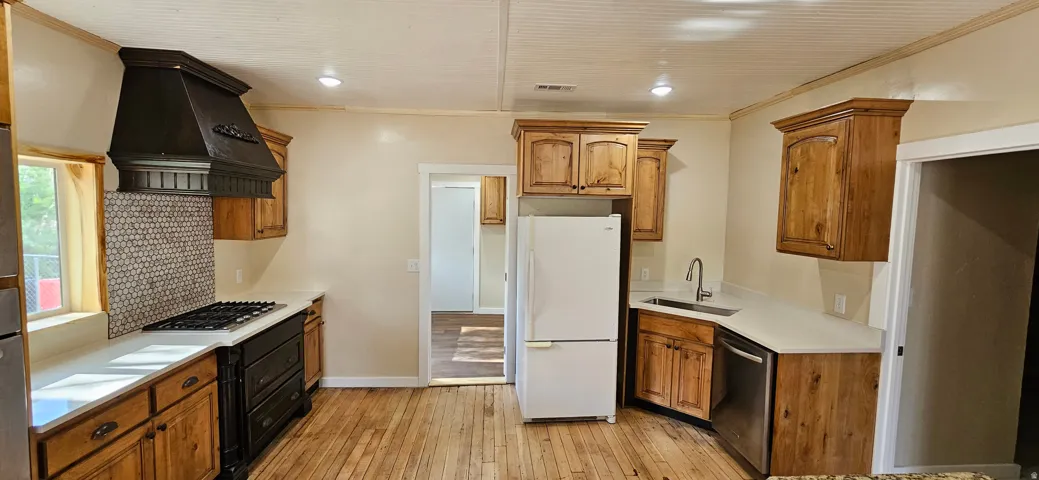 Kitchen featuring wood-finish flooring, light-toned cabinetry, light-toned countertops, a built-in gas range, and a decorative range hood