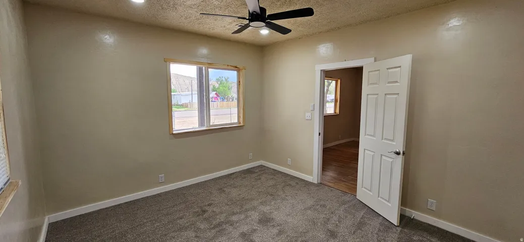 Carpeted room featuring a ceiling fan with integrated lighting, a window with natural wood trim, and a white paneled interior door