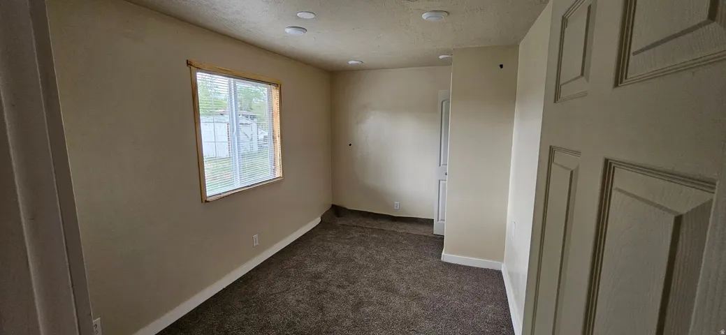 Spacious room featuring neutral paint, brown carpeting, and a window with wood trim