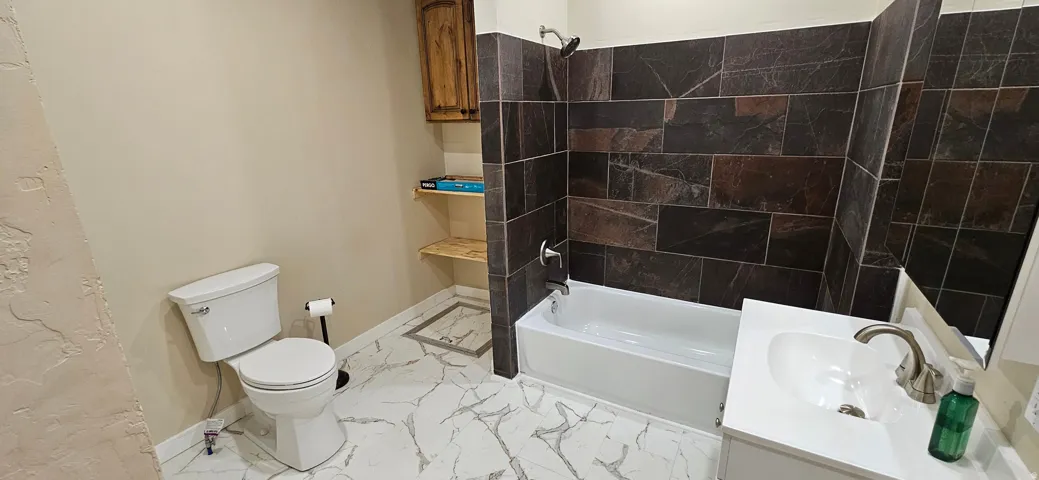 Bathroom featuring white bathtub with dark tiled surround, white vanity with basin sink, and wood-finish cabinetry