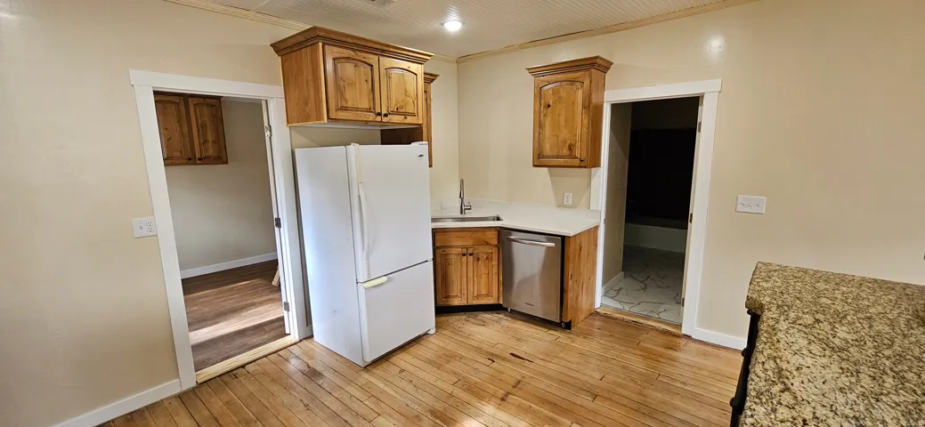 Kitchen featuring natural wood cabinetry, white countertops, stainless steel dishwasher, and wood-finish flooring