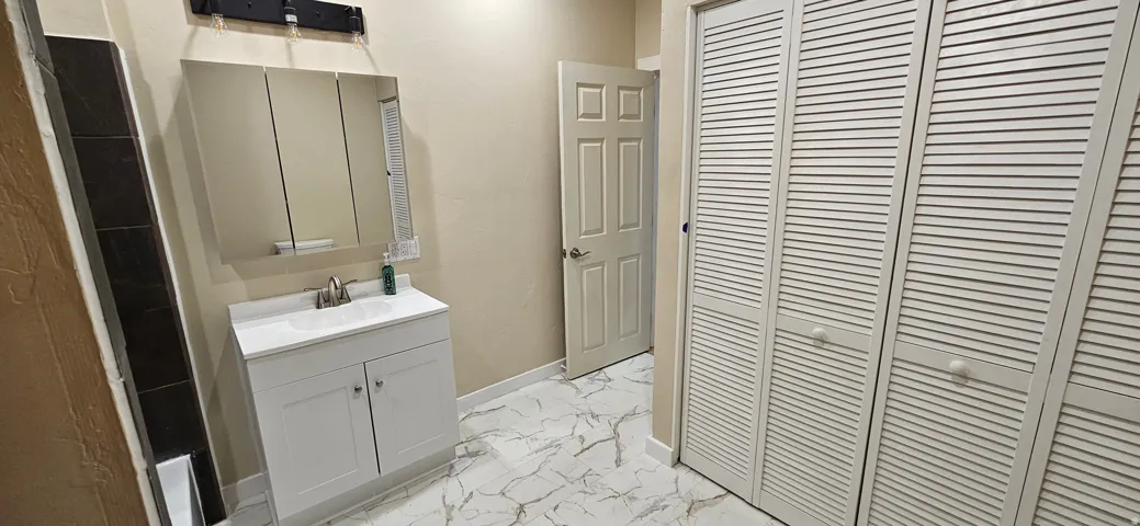 Bathroom featuring a white vanity with integrated sink, tri-fold mirrored medicine cabinet, and a white six-panel door