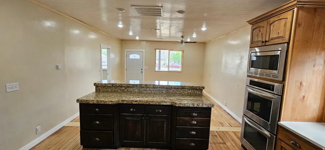 Kitchen island with a granite countertop, dark wood cabinetry, and recessed lighting