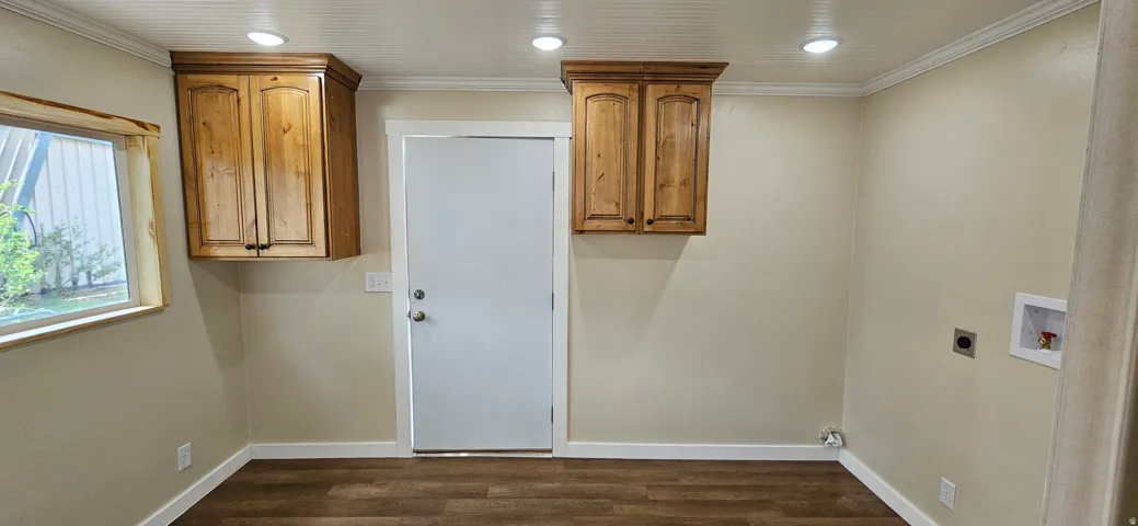 Utility space featuring wood-finish flooring, two upper wood cabinetry units, a bright window with wood trim, recessed ceiling lighting, and a white beadboard ceiling