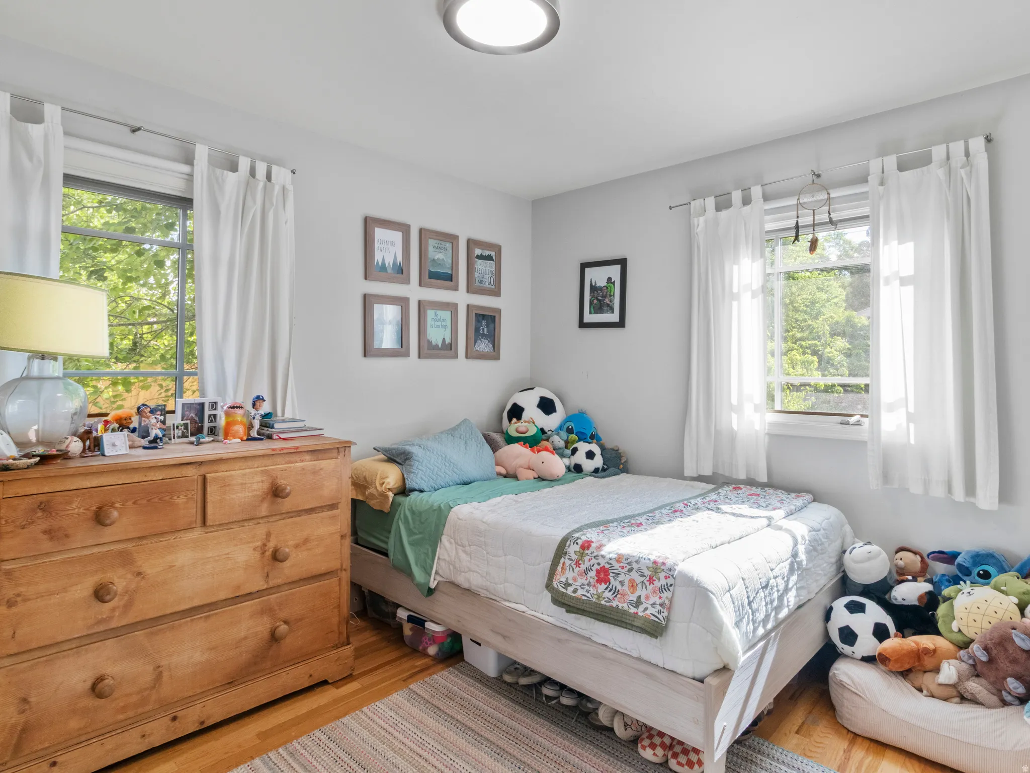 Light-filled room featuring hardwood flooring, white walls, and two multi-pane windows with white curtains