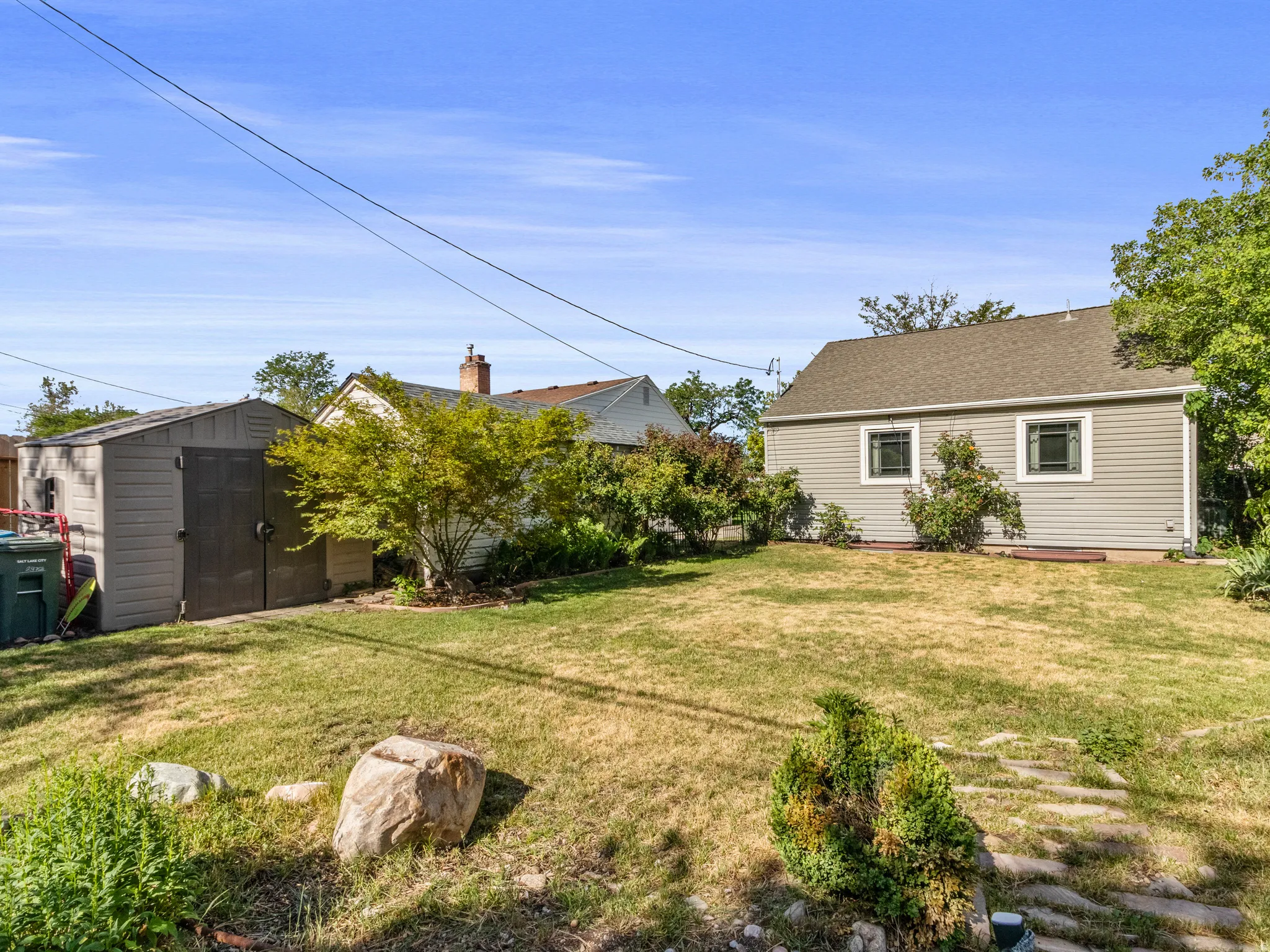 Expansive grassy yard featuring a stone pathway, mature plantings, and a detached storage shed