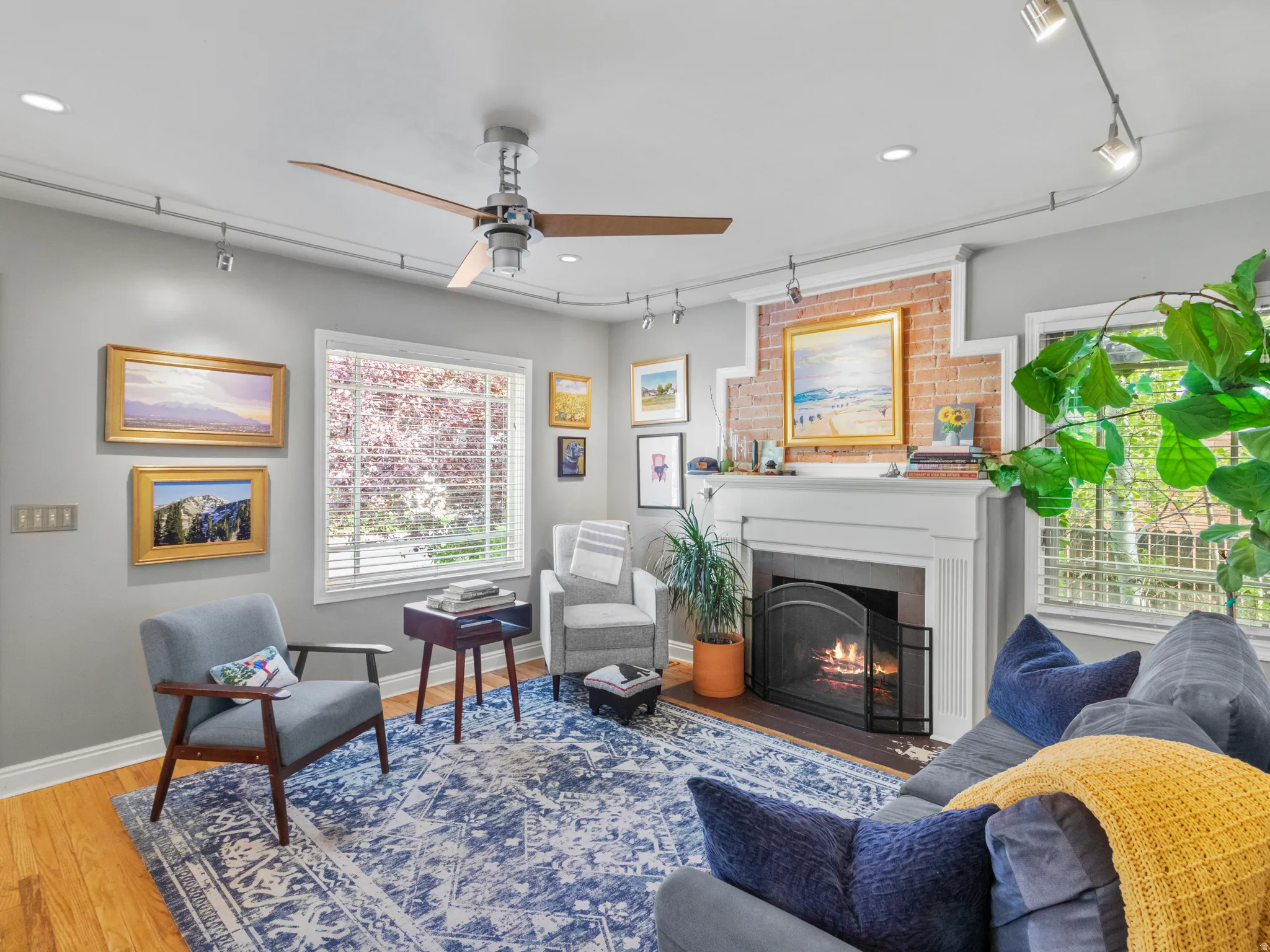 Living area featuring a brick fireplace with a white mantel, wood-finish flooring, and track lighting