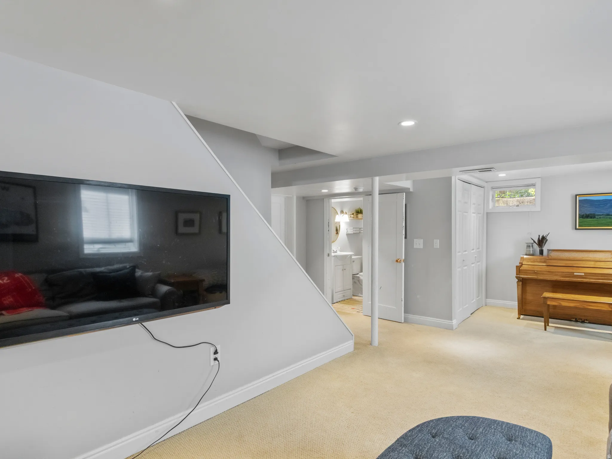 Carpeted lower-level room featuring recessed lighting, a built-in storage closet with bifold doors, a small window, and a built-in media wall