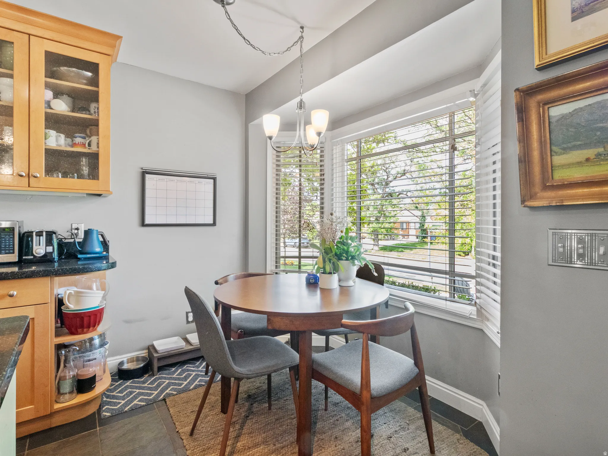 Breakfast nook featuring a bay window with blinds, a multi-light chandelier, a round wood table, and light wood cabinetry with glass-front uppers