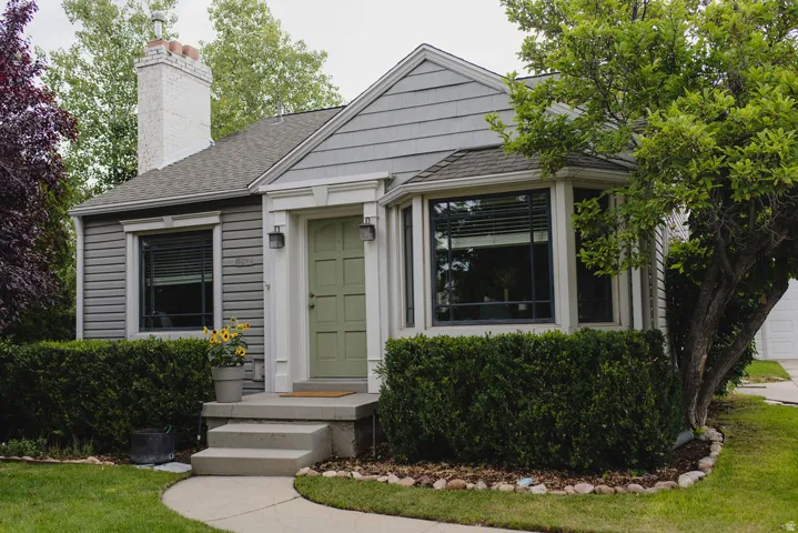 Inviting curb appeal featuring a sage green paneled door, gray horizontal siding, a white brick chimney, and a bay window