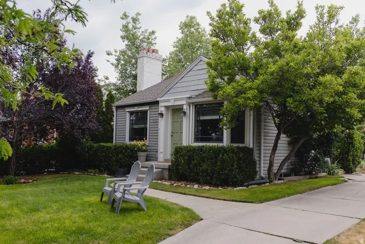 Charming single-story residence with gray siding, a prominent white brick chimney, and a light green entry door