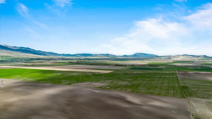 Expansive agricultural landscape featuring diverse cultivation patterns, distant mountain ranges, and power line infrastructure
