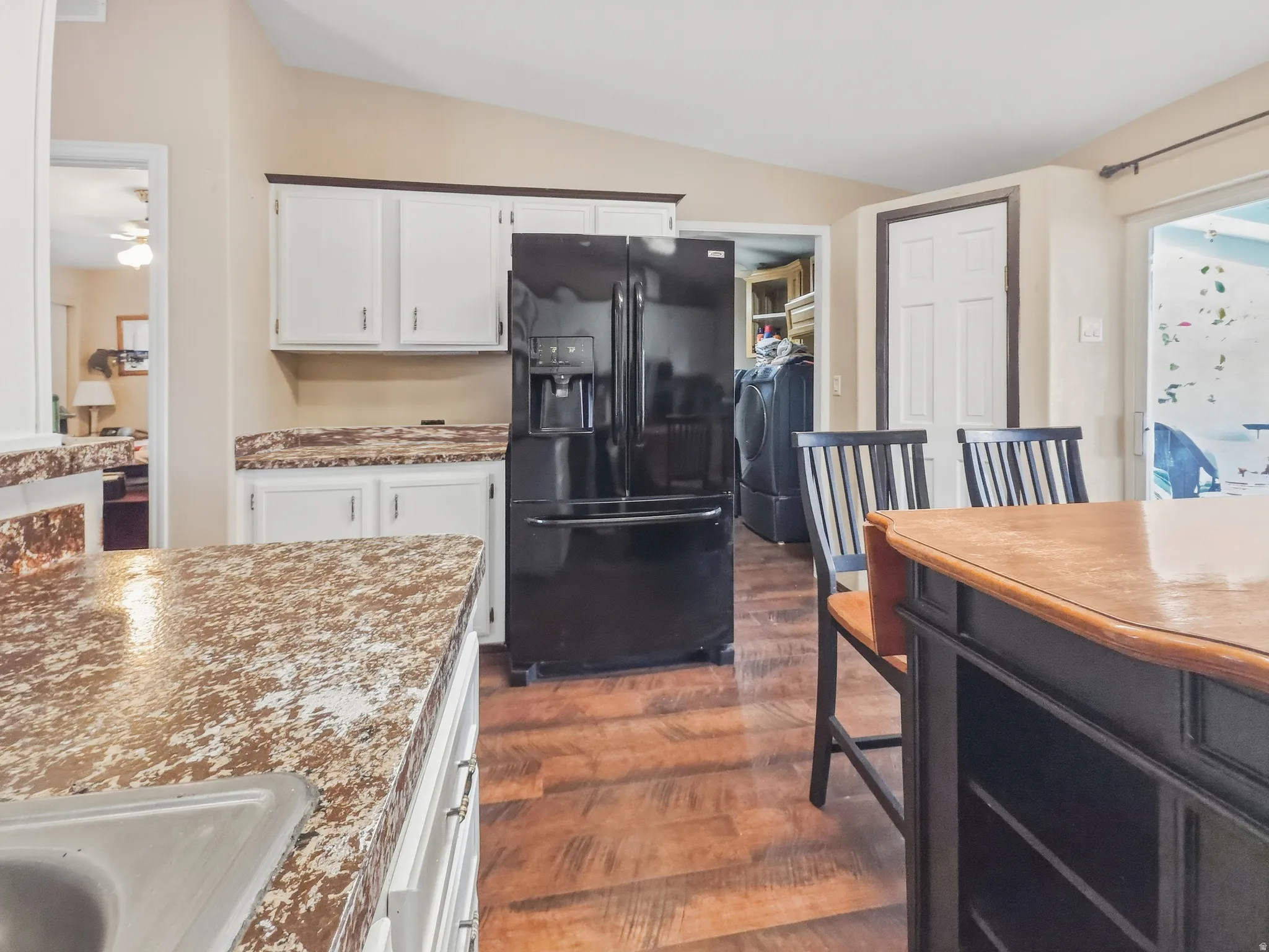 Kitchen featuring white cabinetry with dark hardware, speckled countertops, wood-finish flooring, and a black refrigerator