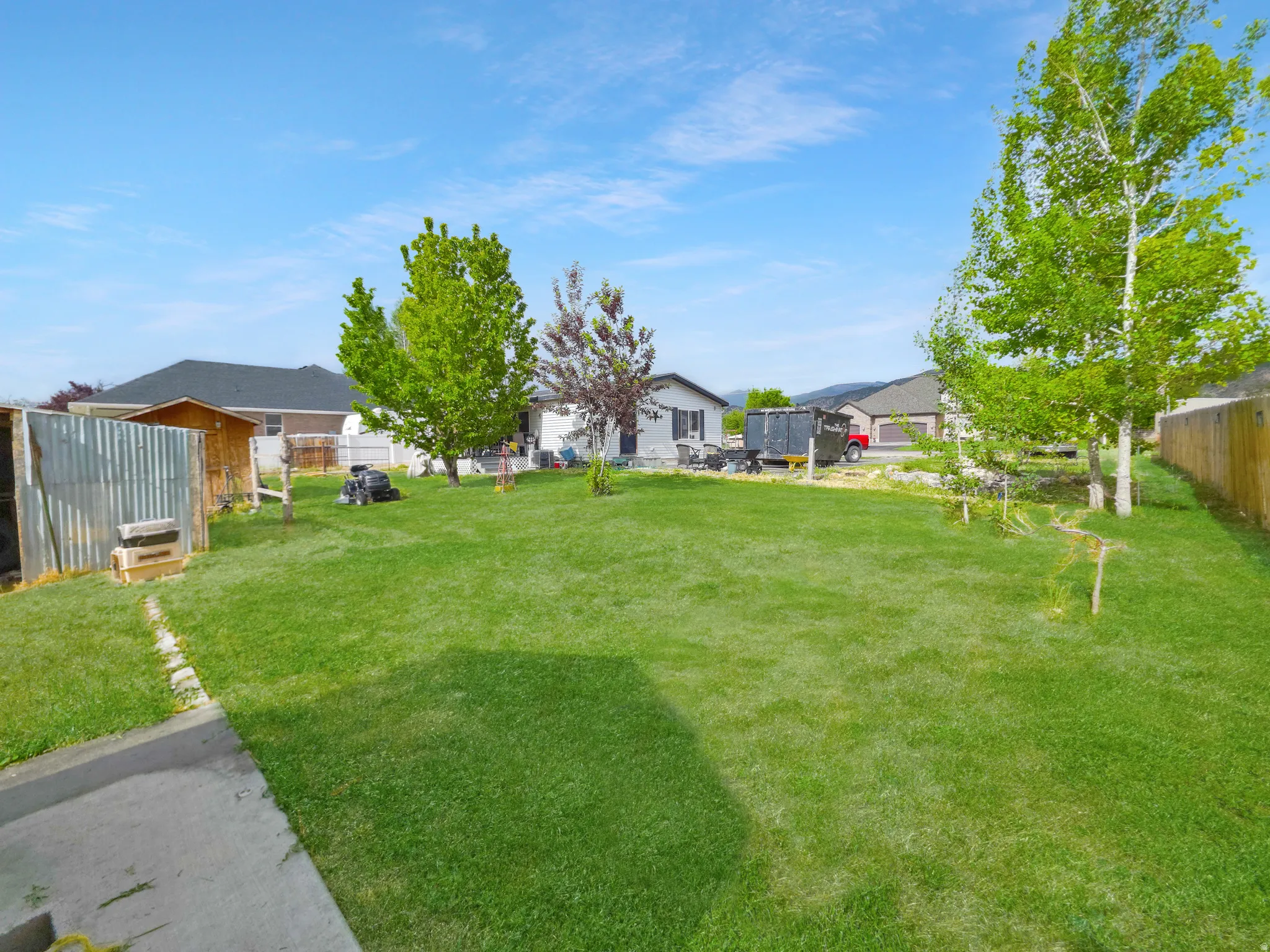 Expansive green lawn with mature trees and a wooden privacy fence