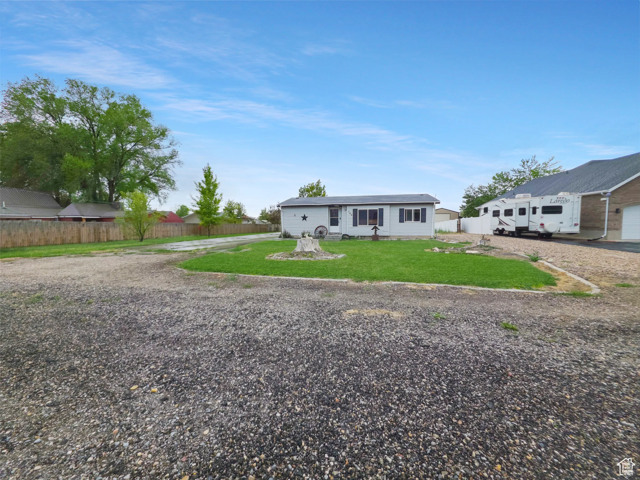 Gravel driveway offering ample parking, with a manicured front lawn and mature trees