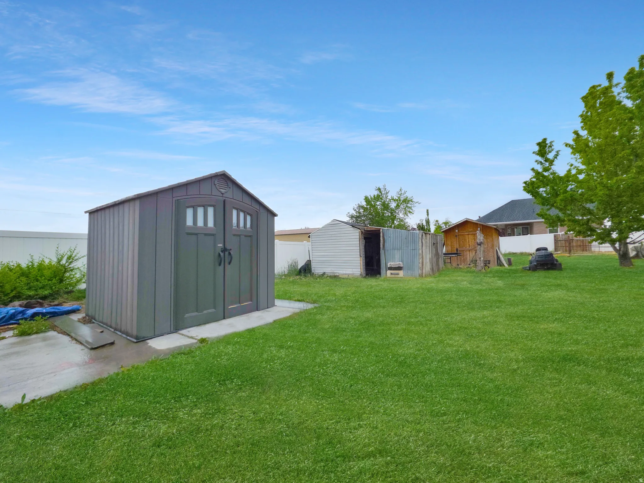 Expansive green space featuring a large storage shed with double doors and a concrete pad