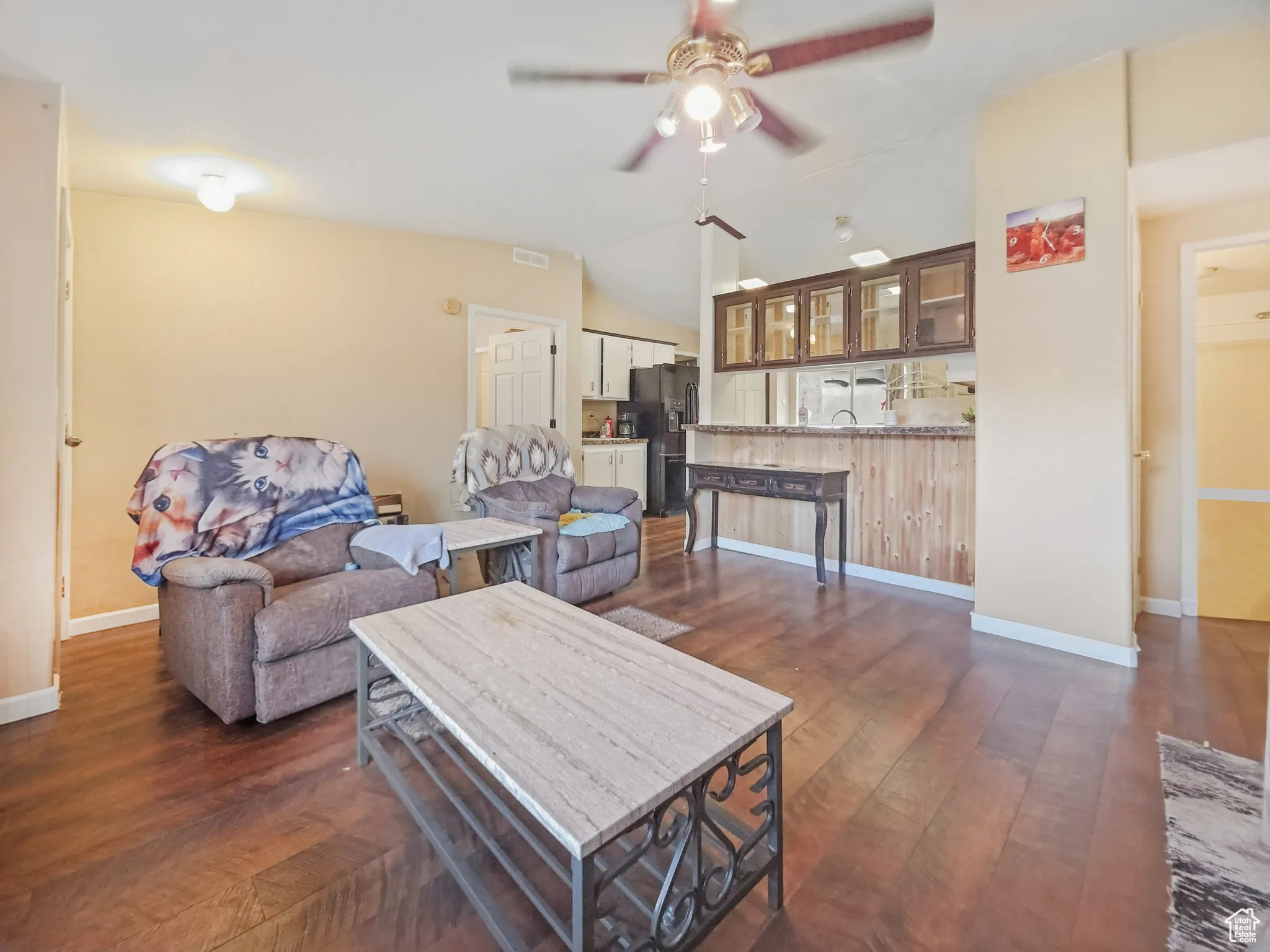 Open-concept living area featuring wood-finish flooring, a ceiling fan with integrated lighting, and a breakfast bar with wood paneling