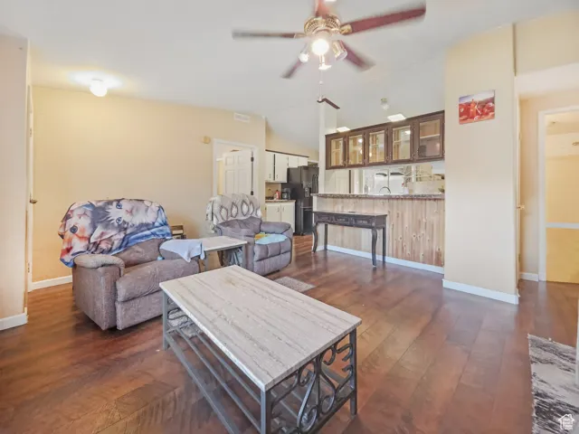 Open-concept living area featuring wood-finish flooring, a ceiling fan with integrated lighting, and a breakfast bar with wood paneling