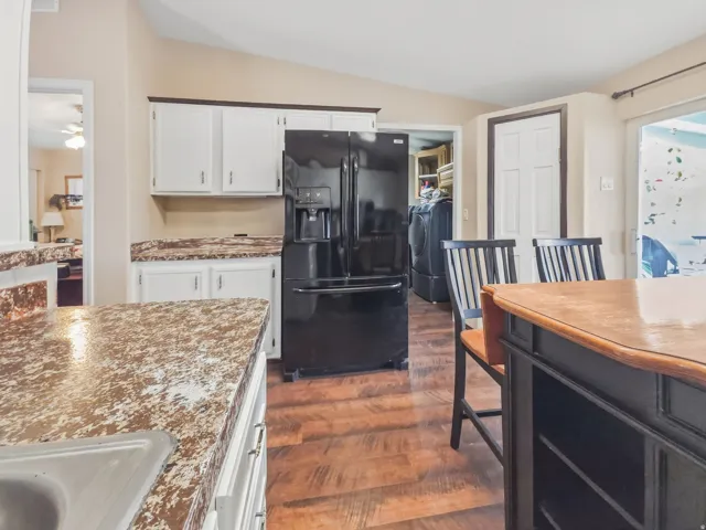Kitchen featuring white cabinetry with dark hardware, speckled countertops, wood-finish flooring, and a black refrigerator