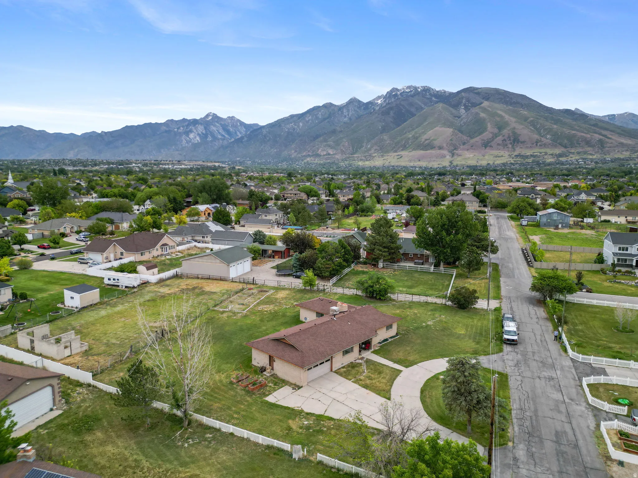 Expansive lot featuring a single-story residence with a brown roof and a white picket fence perimeter