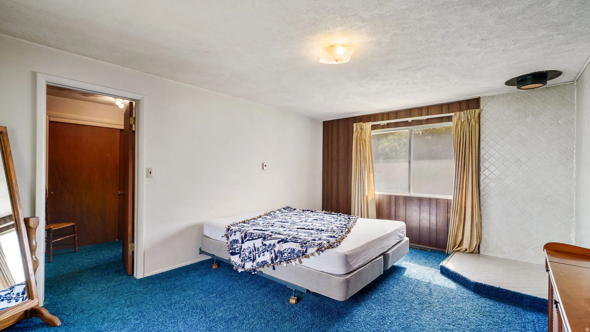 Room featuring blue carpet flooring, a window with horizontal blinds and drapes, and a mixture of white and wood paneling on the walls