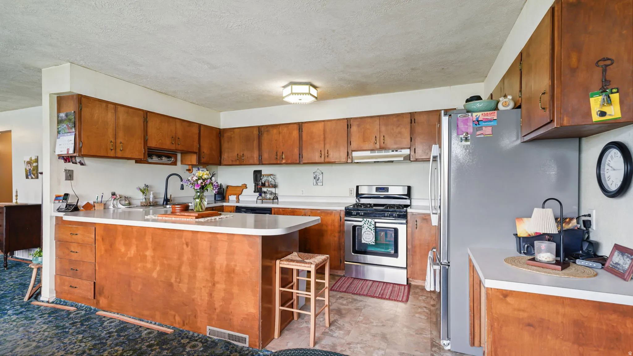 Kitchen featuring wood cabinetry, light countertops, stainless steel appliances, and a central island with an extended counter