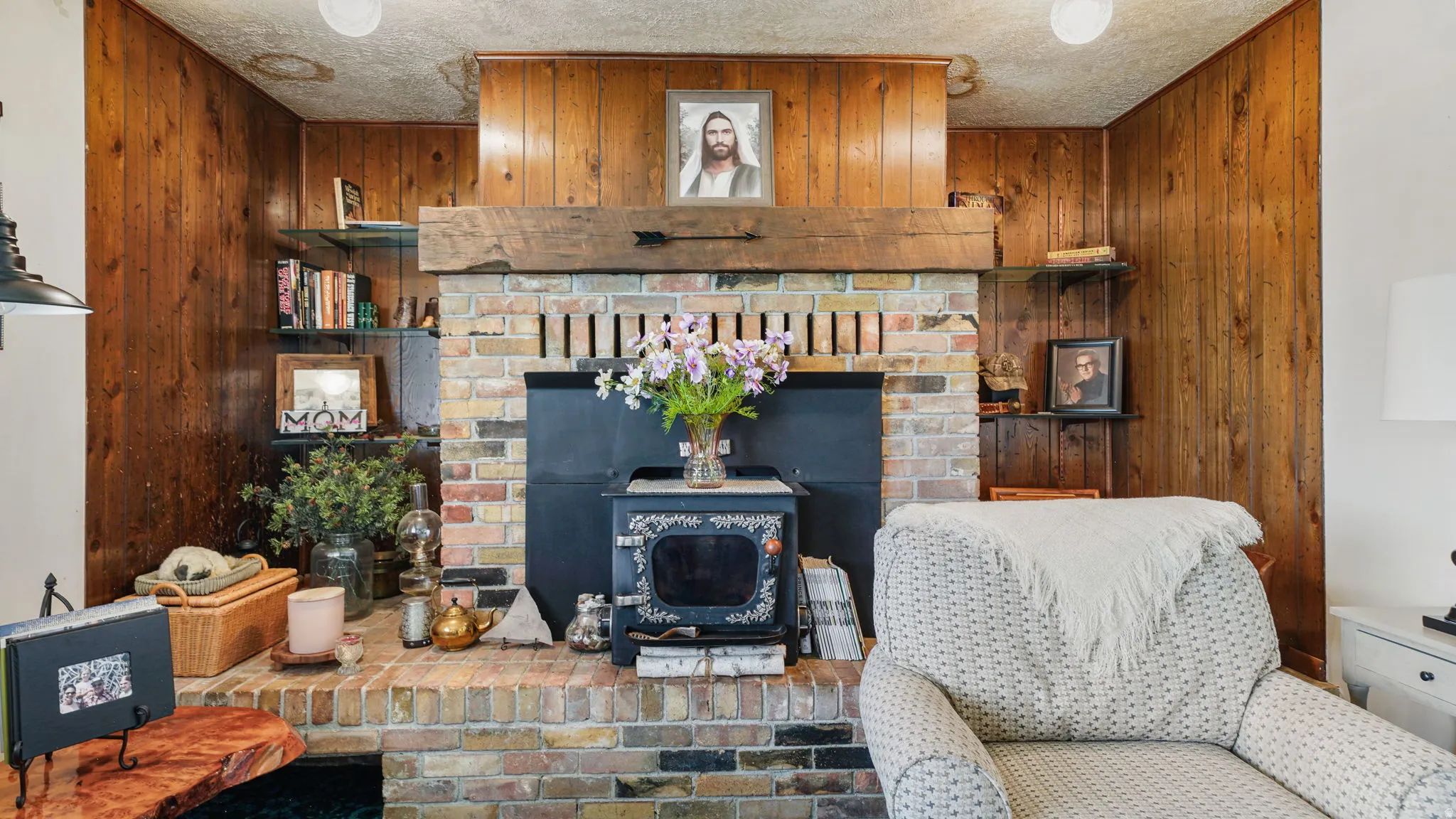 Brick fireplace with a substantial wood mantel, wood paneling, and a black wood-burning stove