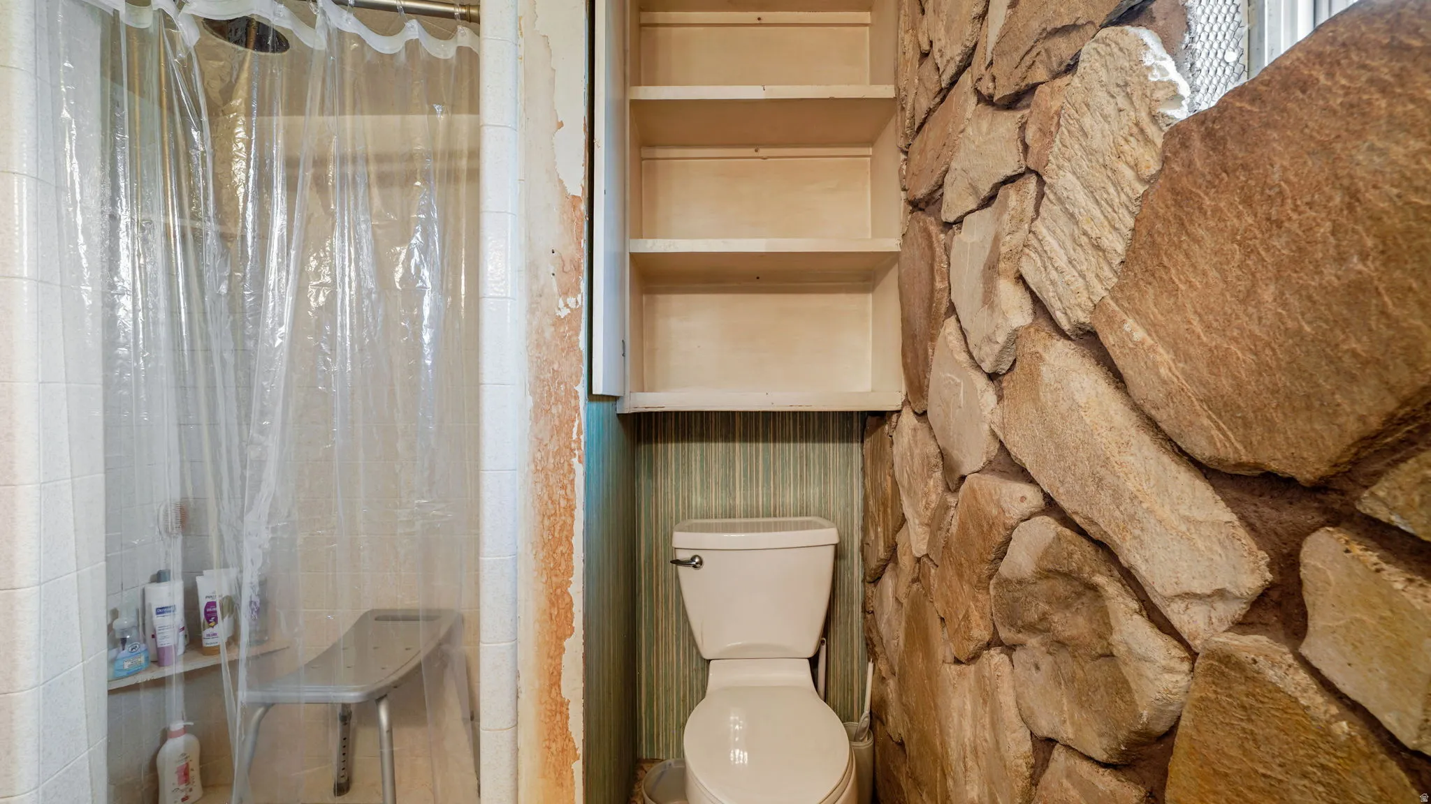 Bathroom featuring a stone accent wall and a tiled shower stall