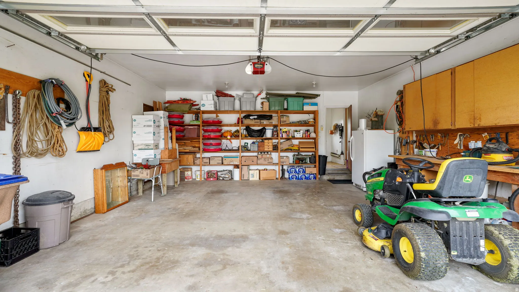 Spacious garage featuring a concrete floor, overhead garage door with window panels, built-in shelving, wall-mounted cabinetry, and a workbench