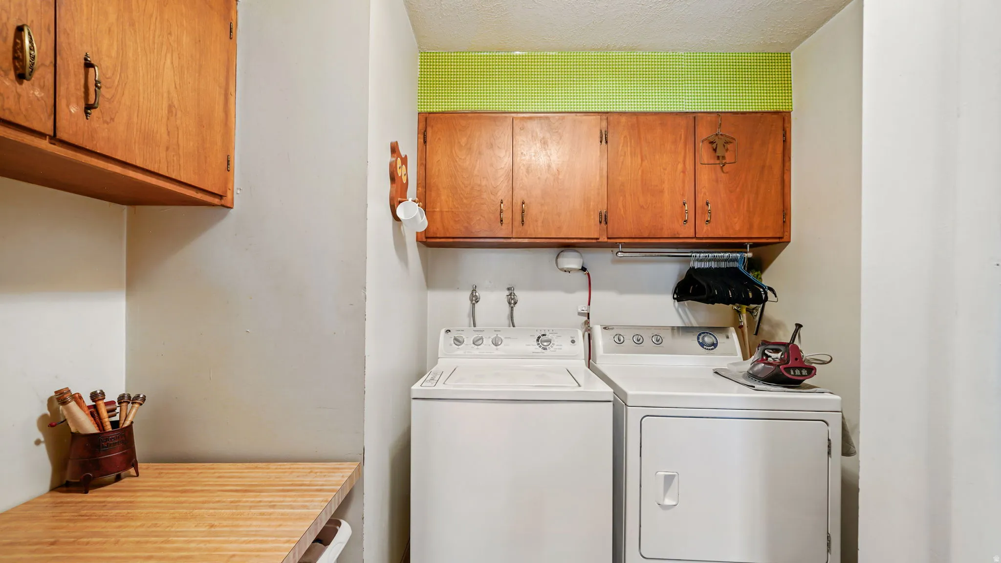 Dedicated laundry area featuring a washer and dryer, wood-finish cabinetry, a wood-finish countertop, and a wall-mounted hanging rod