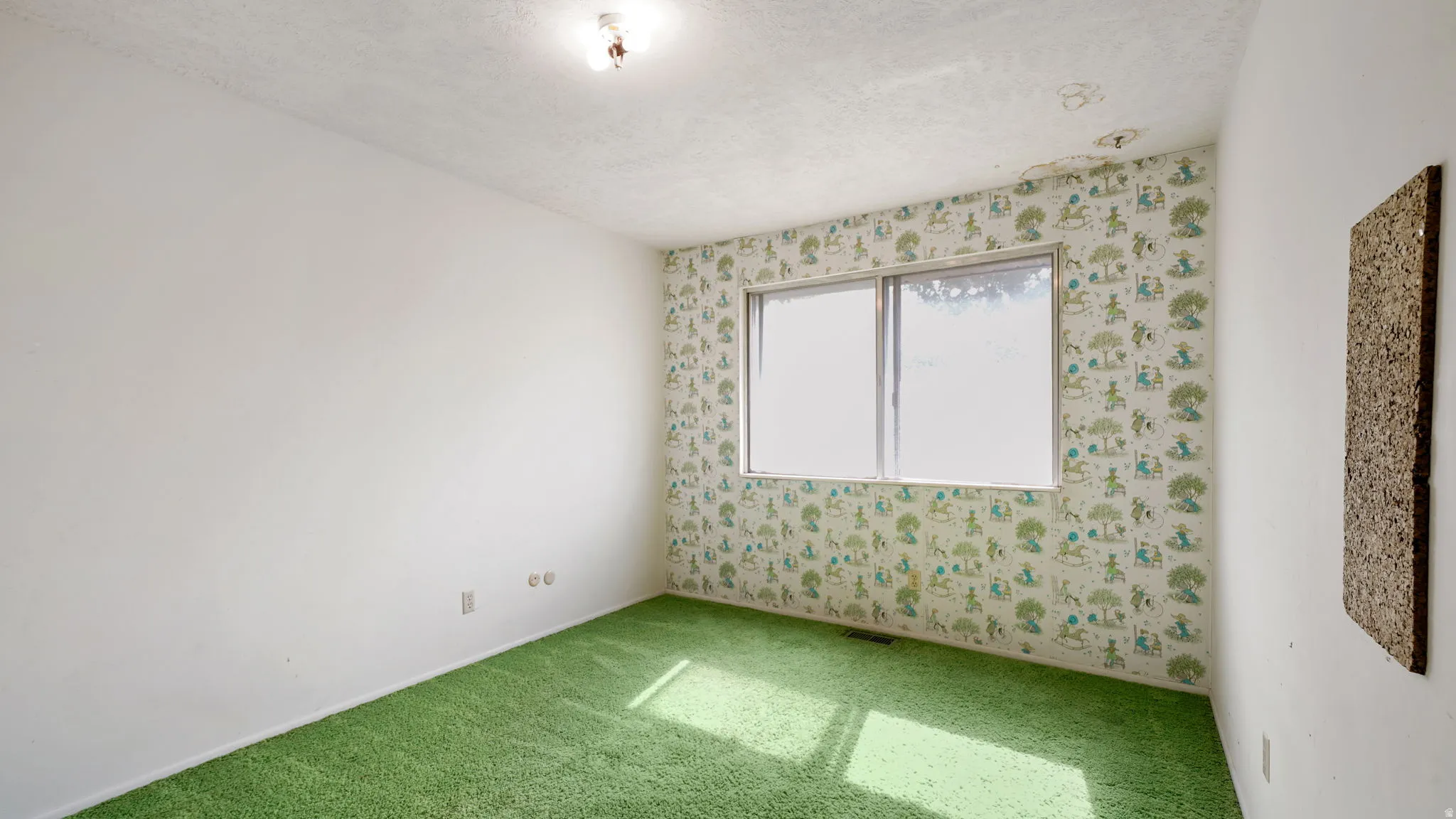 Interior room featuring a large window, patterned wallpaper, a single ceiling light fixture, and green carpeting