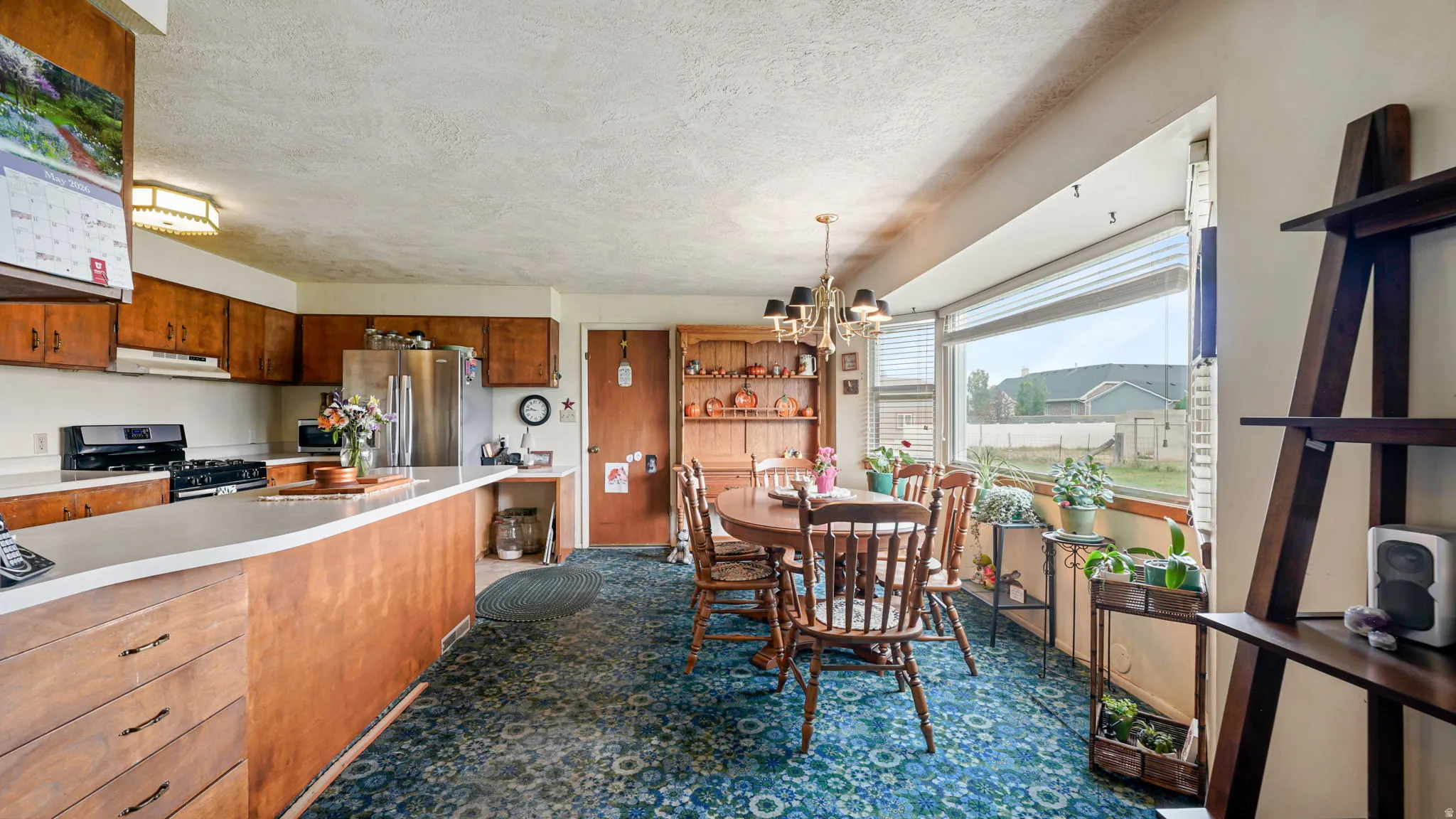 Kitchen and dining area featuring wood cabinetry, stainless steel refrigerator, white countertops, and a dining space with a large window